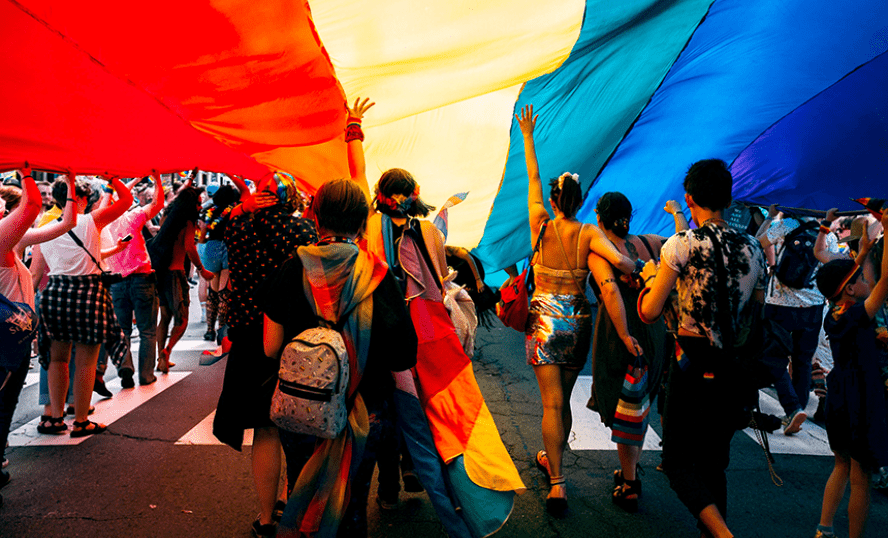 Personer som står under en jättestor HBTQ-flagga.