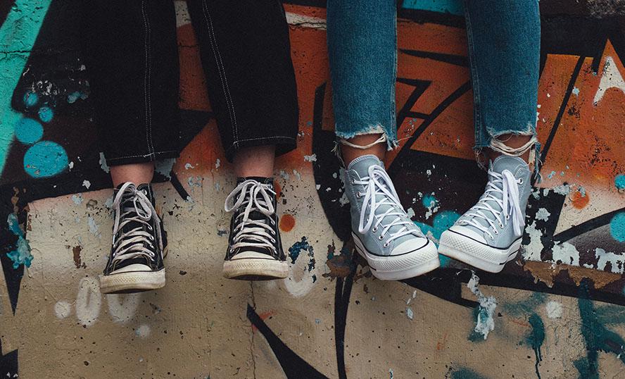 Två ungdomars fötter i sneakers hänger ned framför en graffitimålad vägg