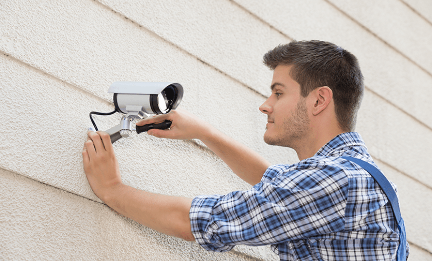 Man som sätter upp övervakningskamera på vägg.