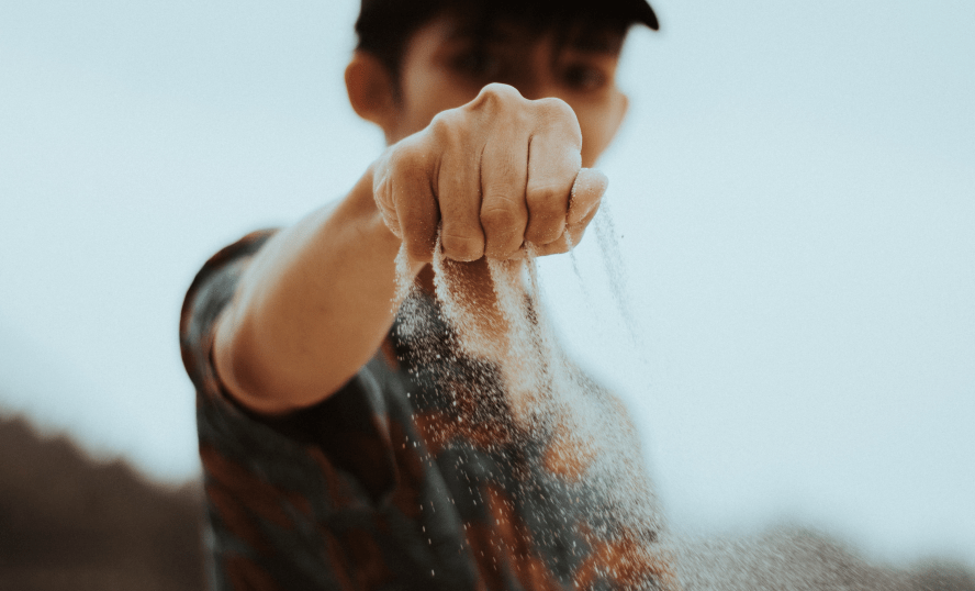 Ung kille som håller fram hand där det rinner ut sand