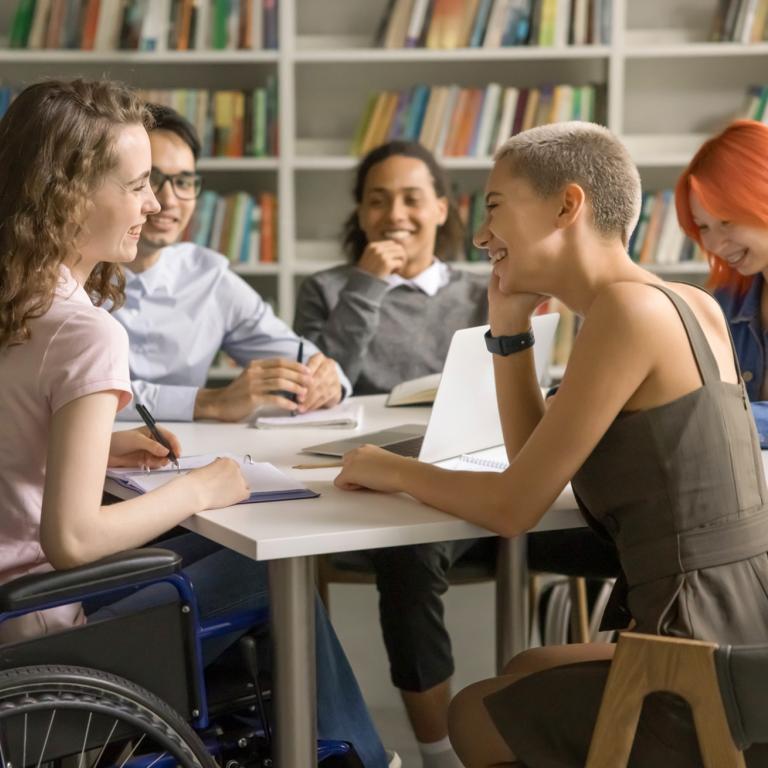 Unga personer som sitter och samtalar runt ett bord i ett bibliotek