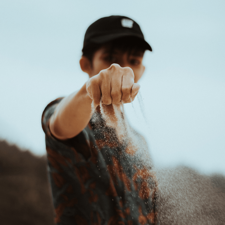 Ung kille som håller fram hand där det rinner ut sand